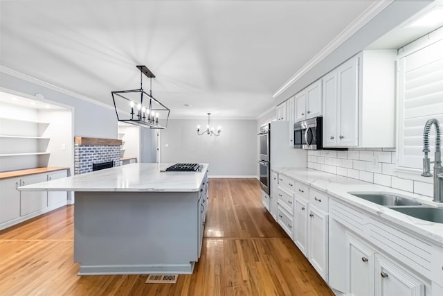 kitchen with a sink, white cabinets, appliances with stainless steel finishes, a center island, and crown molding