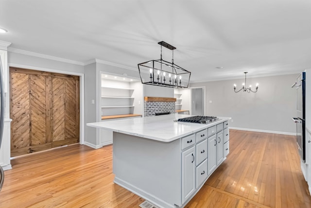 kitchen with crown molding, stainless steel gas stovetop, light wood finished floors, and a kitchen island