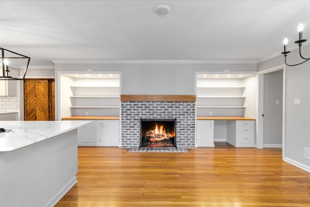 unfurnished living room featuring built in features, crown molding, a fireplace, built in desk, and light wood-style floors