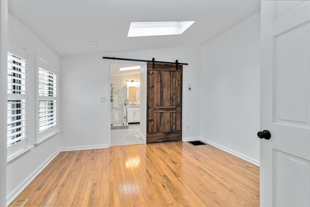 spare room with visible vents, a barn door, light wood-type flooring, vaulted ceiling with skylight, and baseboards