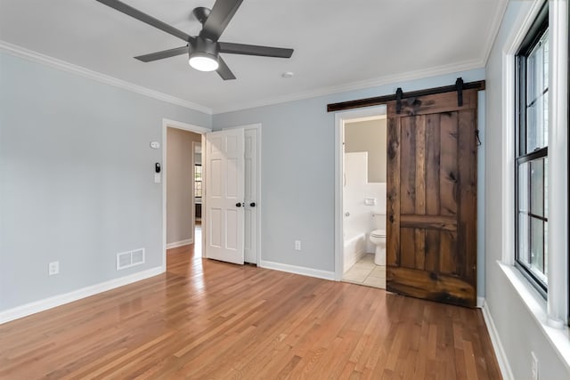 unfurnished bedroom featuring light wood finished floors, visible vents, a barn door, ornamental molding, and baseboards