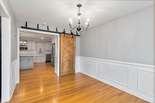 unfurnished dining area with light wood-style floors, a sink, an inviting chandelier, and a barn door