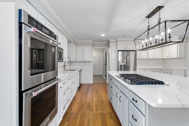 kitchen featuring light wood-style flooring, appliances with stainless steel finishes, ornamental molding, white cabinets, and a sink