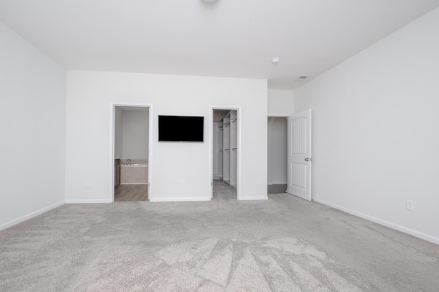 unfurnished bedroom featuring carpet, a walk in closet, baseboards, and ensuite bathroom