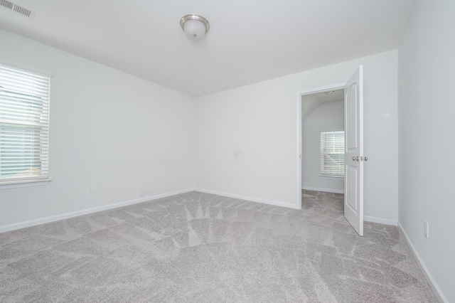 spare room with visible vents, vaulted ceiling, light carpet, and baseboards