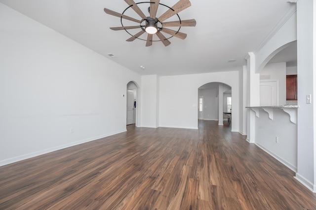 unfurnished living room with dark wood-style floors, ceiling fan, arched walkways, and baseboards