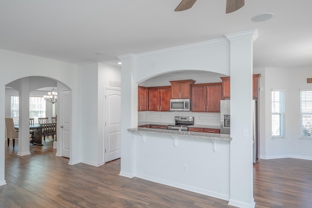 kitchen featuring stainless steel appliances, a healthy amount of sunlight, a kitchen breakfast bar, tasteful backsplash, and dark wood finished floors