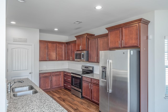 kitchen featuring visible vents, appliances with stainless steel finishes, dark wood-type flooring, light stone countertops, and a sink