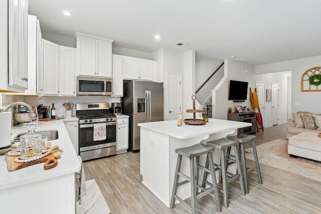 kitchen featuring a sink, white cabinets, open floor plan, light countertops, and appliances with stainless steel finishes