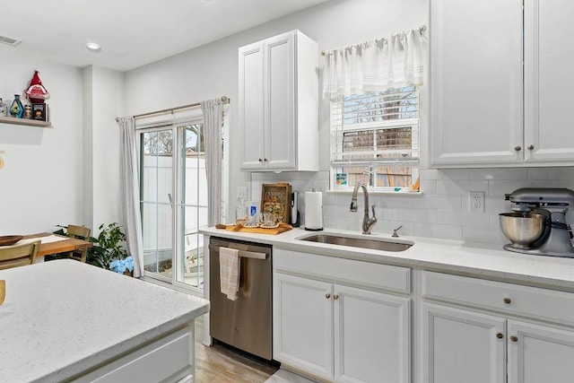 kitchen featuring decorative backsplash, white cabinetry, a sink, and stainless steel dishwasher