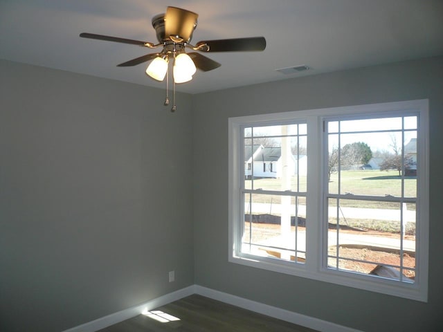 empty room with a ceiling fan, visible vents, dark wood finished floors, and baseboards