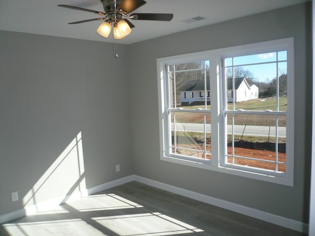 empty room featuring a ceiling fan, dark wood-style flooring, visible vents, and baseboards