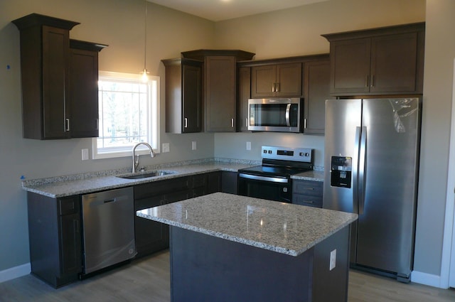 kitchen featuring a kitchen island, appliances with stainless steel finishes, light stone counters, light wood-style floors, and a sink