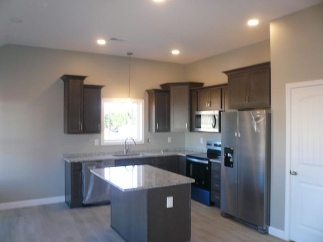 kitchen with a sink, a center island, dark brown cabinets, appliances with stainless steel finishes, and light stone countertops