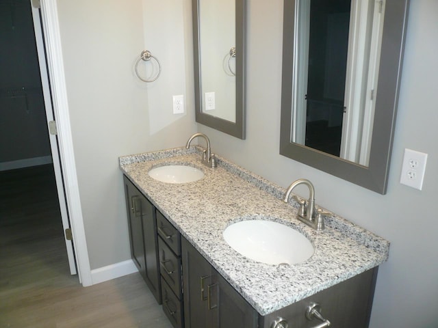 full bathroom featuring double vanity, baseboards, a sink, and wood finished floors