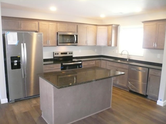 kitchen featuring dark wood finished floors, appliances with stainless steel finishes, a sink, a kitchen island, and dark stone countertops