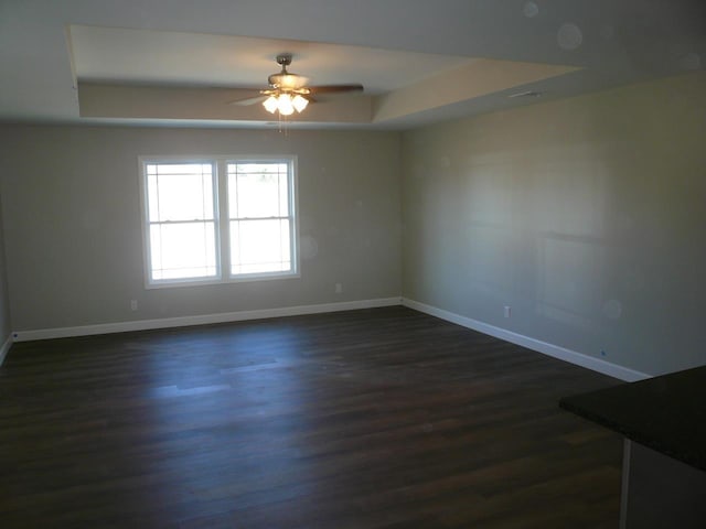 spare room featuring ceiling fan, a tray ceiling, dark wood finished floors, and baseboards