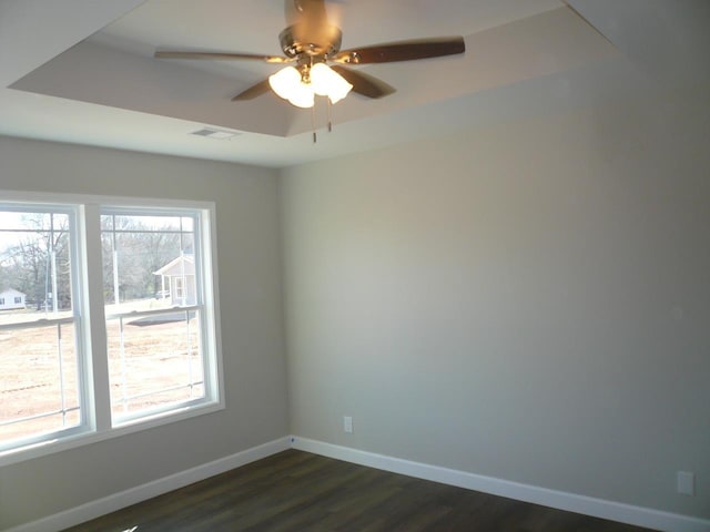 empty room featuring dark wood-style floors, a raised ceiling, visible vents, ceiling fan, and baseboards