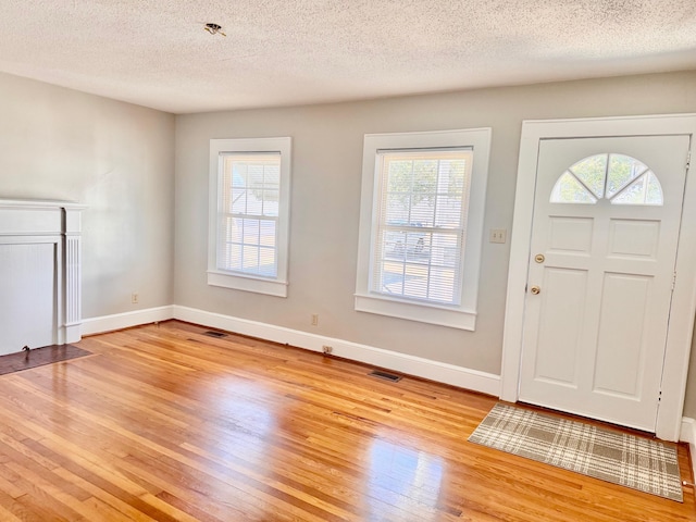 foyer entrance featuring baseboards, a textured ceiling, visible vents, and light wood-style floors