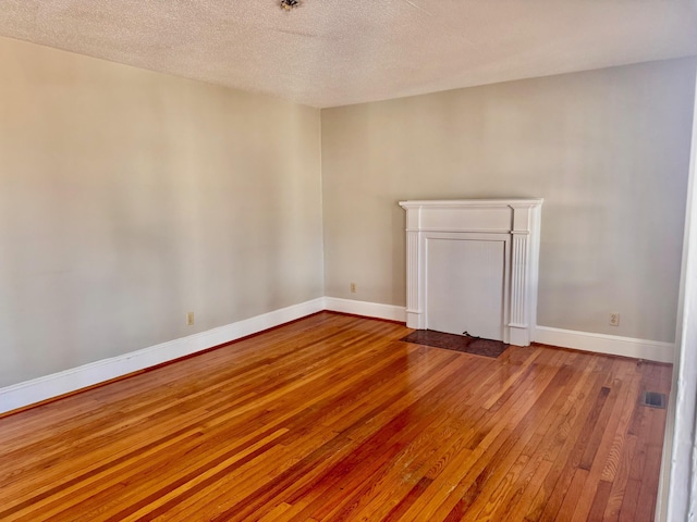 spare room featuring a textured ceiling, hardwood / wood-style flooring, and baseboards