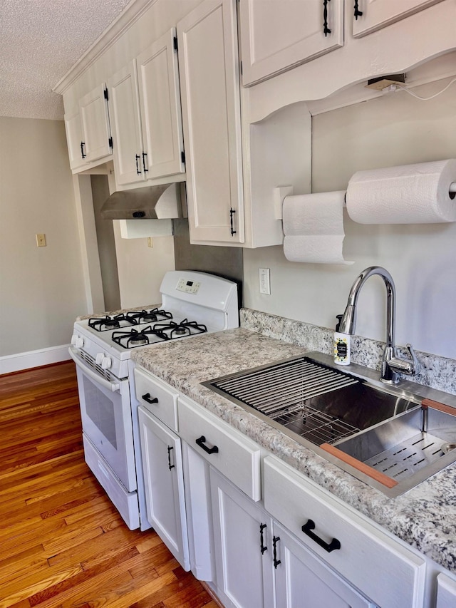 kitchen with under cabinet range hood, a sink, white cabinetry, light wood-type flooring, and white gas range