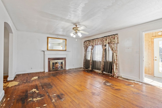 unfurnished living room featuring a brick fireplace, ceiling fan, arched walkways, and hardwood / wood-style floors