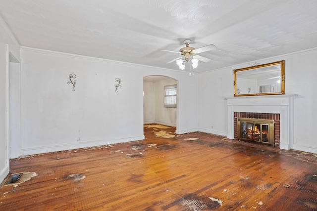 unfurnished living room with arched walkways, a ceiling fan, ornamental molding, a brick fireplace, and wood-type flooring