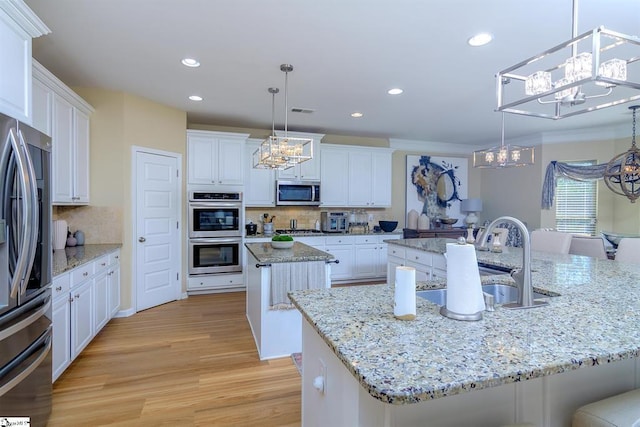 kitchen with a center island with sink, light wood finished floors, stainless steel appliances, white cabinets, and a sink