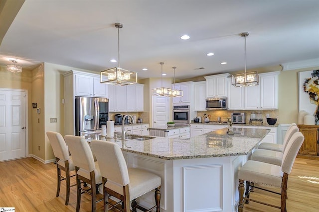 kitchen featuring stainless steel appliances, a spacious island, a sink, light wood-style floors, and backsplash