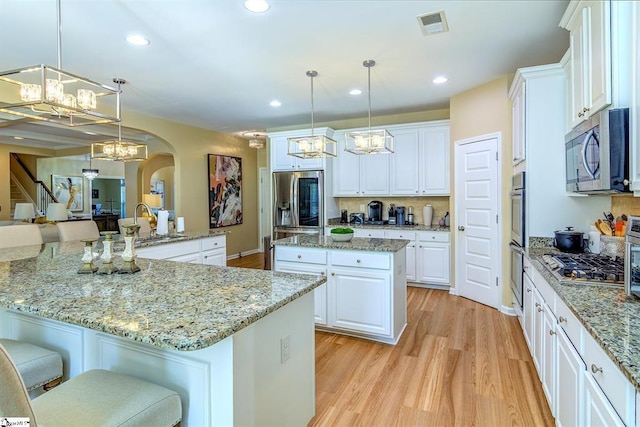 kitchen with a large island, stainless steel appliances, visible vents, light wood-style floors, and white cabinetry