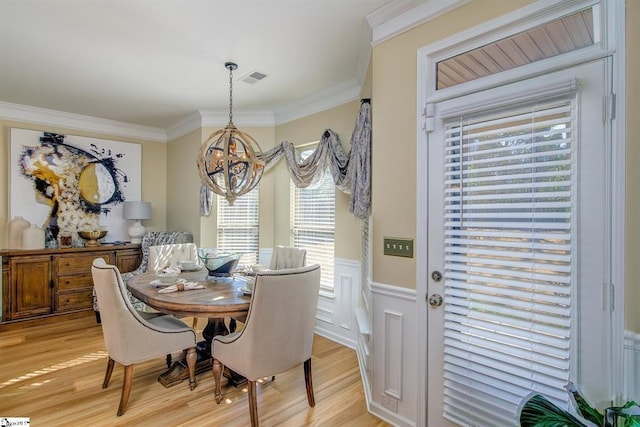 dining area featuring wainscoting, crown molding, light wood-style flooring, and an inviting chandelier