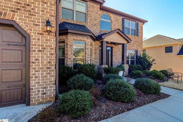 entrance to property featuring a garage and brick siding