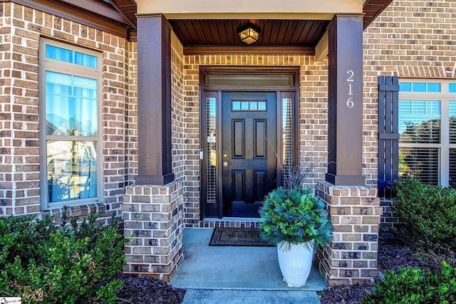 view of exterior entry with a porch and brick siding