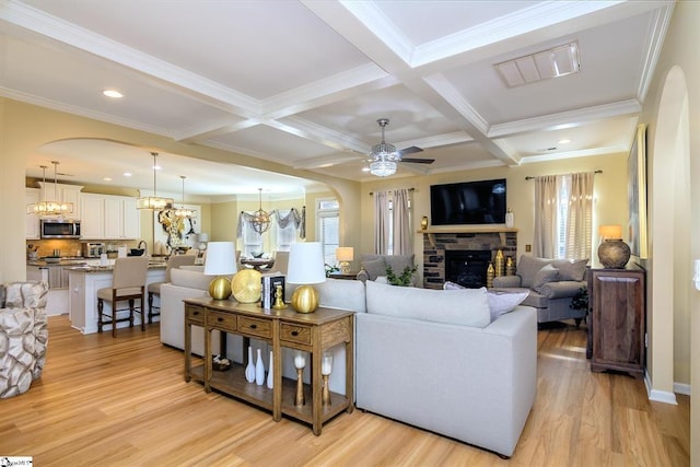 living room with arched walkways, light wood finished floors, a fireplace, and visible vents