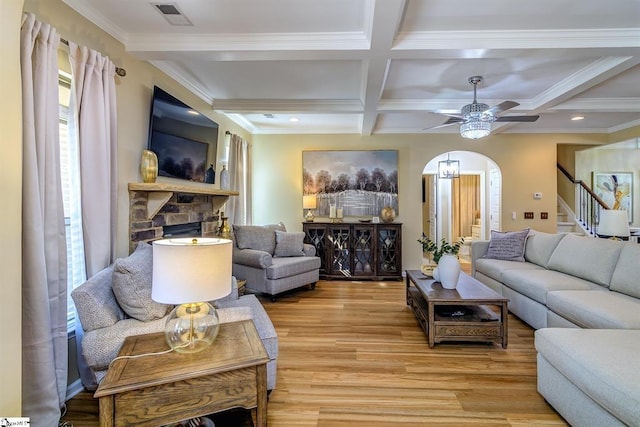 living area featuring arched walkways, coffered ceiling, visible vents, light wood finished floors, and beamed ceiling