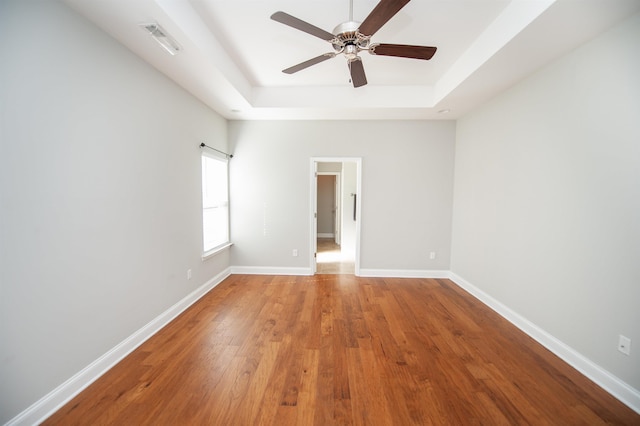 empty room featuring wood finished floors, a raised ceiling, visible vents, and baseboards