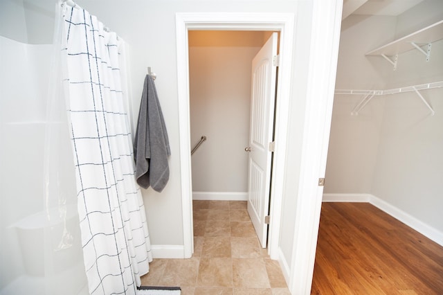 full bathroom featuring curtained shower, a walk in closet, tile patterned flooring, and baseboards