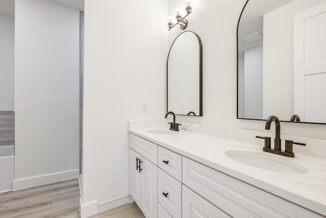 bathroom with double vanity, baseboards, a sink, and wood finished floors