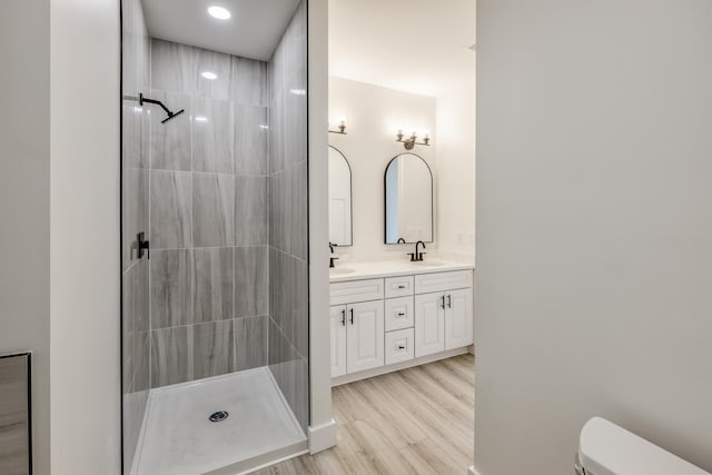 bathroom with toilet, wood finished floors, a sink, a tile shower, and double vanity