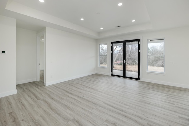 empty room featuring light wood-type flooring, baseboards, a tray ceiling, and french doors