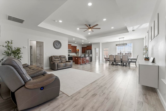 living area with a tray ceiling, visible vents, light wood finished floors, and recessed lighting