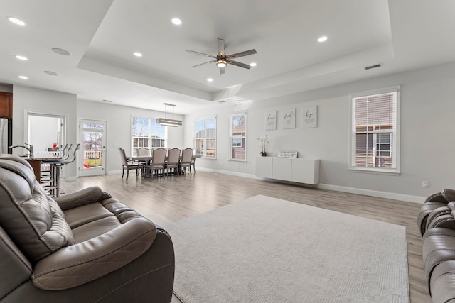 living area featuring light wood-type flooring, visible vents, a raised ceiling, and recessed lighting