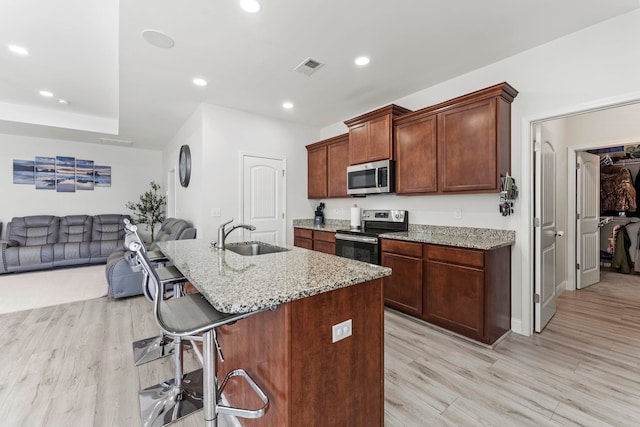 kitchen with visible vents, appliances with stainless steel finishes, a breakfast bar, light wood-type flooring, and a sink