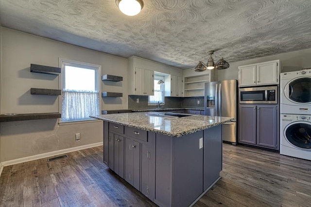 kitchen featuring open shelves, stacked washer / drying machine, appliances with stainless steel finishes, dark wood-type flooring, and a kitchen island