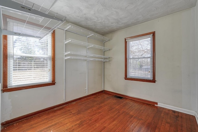 empty room with baseboards, wood-type flooring, visible vents, and a healthy amount of sunlight