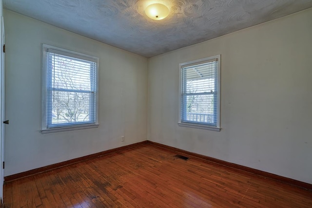 spare room featuring a textured ceiling, hardwood / wood-style flooring, visible vents, and baseboards