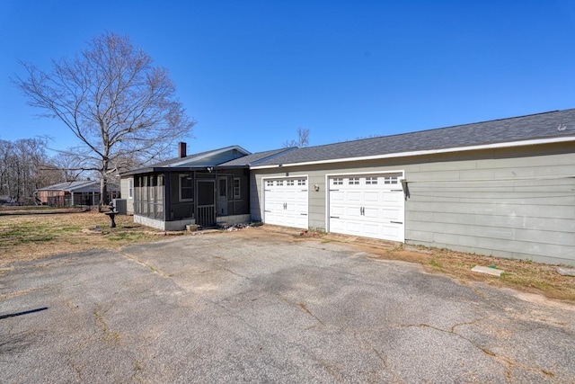 exterior space with aphalt driveway, a sunroom, and a garage