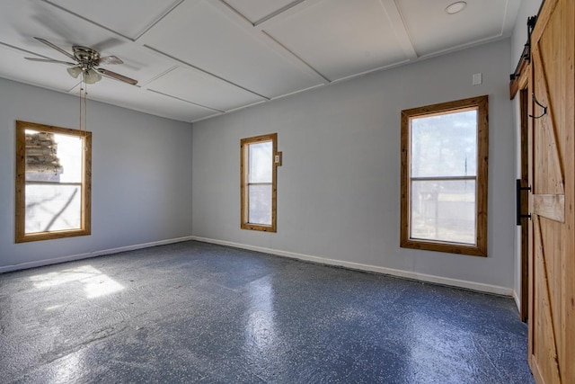 empty room featuring baseboards, a barn door, a ceiling fan, and a healthy amount of sunlight