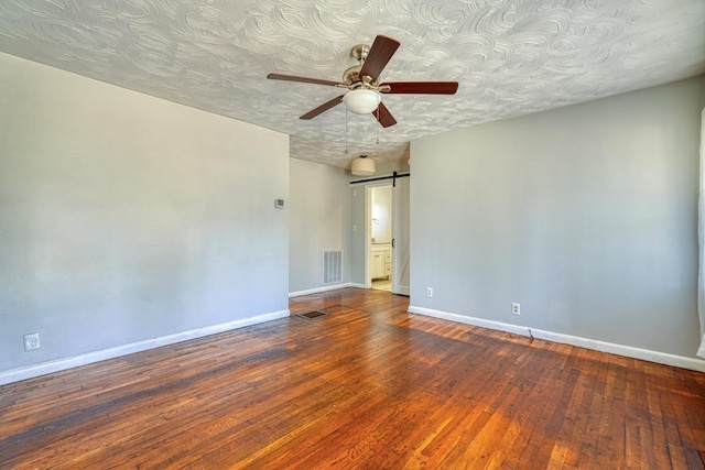 empty room featuring a barn door, visible vents, wood-type flooring, and baseboards