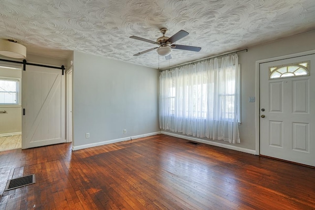 foyer entrance featuring hardwood / wood-style floors, a barn door, visible vents, and a ceiling fan